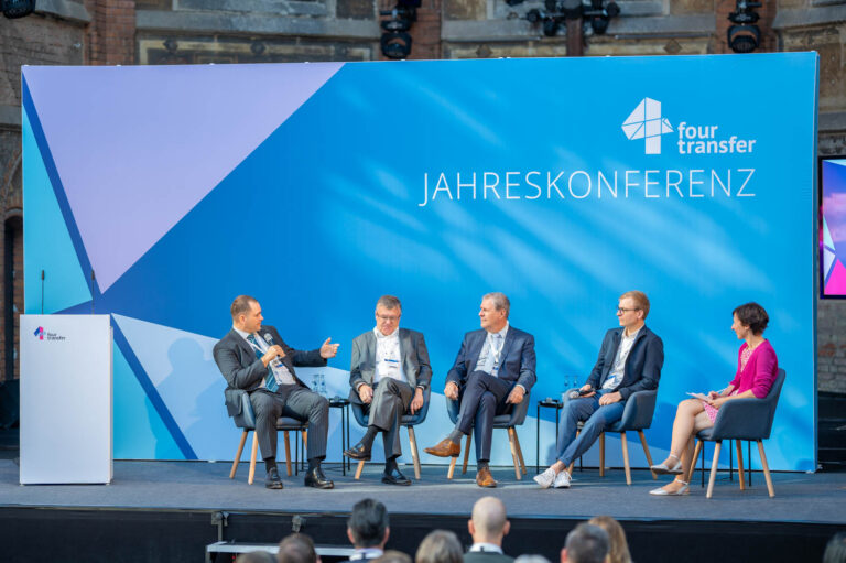 4 Männer diskutieren auf einem Podium mit einer Moderatorin