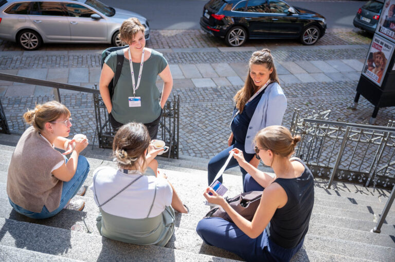 5 Frauen stehen und sitzen auf einer Treppe im Sonnenschein und unterhalten sich