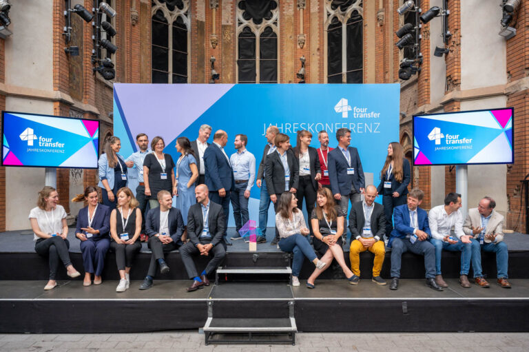 Gruppenbild mit ca. 25 Personen auf einer Bühne vor einer Pressewand 