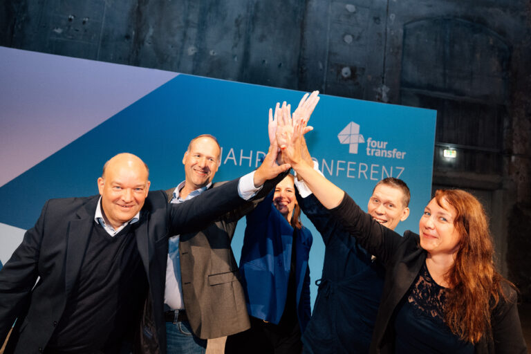 5 Menschen geben sich ein High-Five vor einer Pressewand 