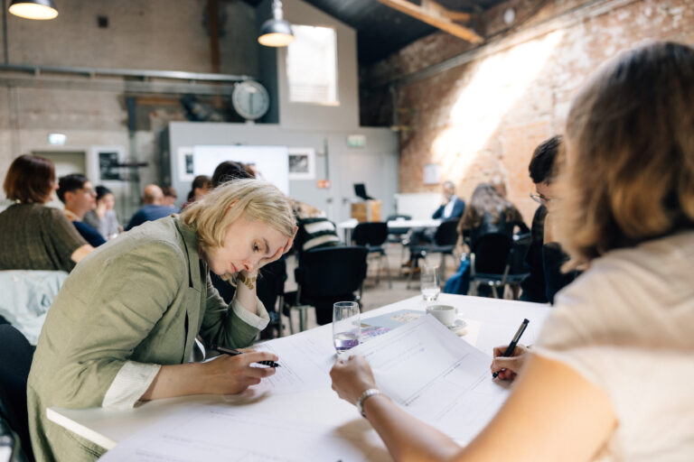 Menschen arbeiten in einem Workshop; alle notieren etwas auf eigenen Arbeitsblättern