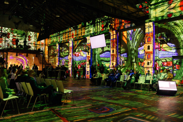 Blick in eine alte Fabrikhalle mit Konferenzsetting, An den Wänden ist immersive, digitale Gestaltung erkennbar